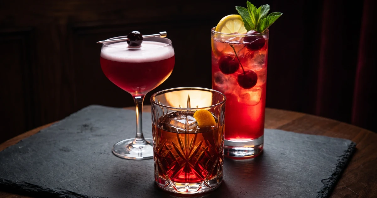 Three LYUBOMIROFF Cherry Liqueur cocktails in different glassware — coupe, rocks glass, and highball glass — glowing deep red against a dark background.